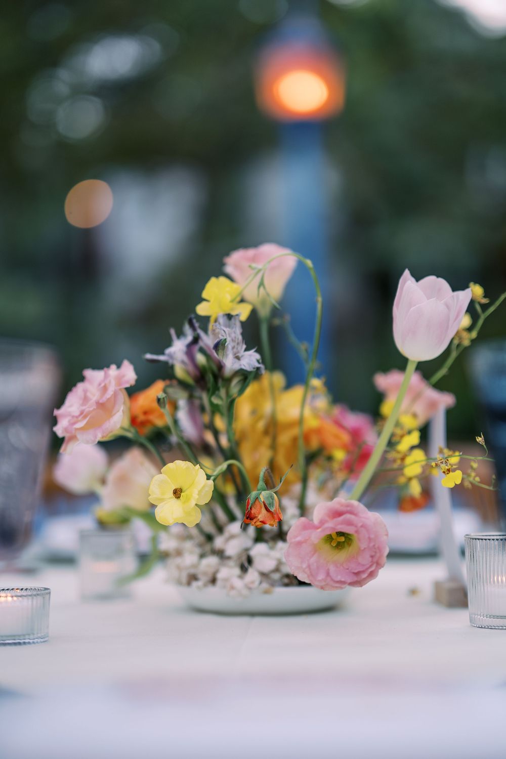 A delicate floral centerpiece with pink and yellow blooms in soft focus with candlelight glowing in the background.