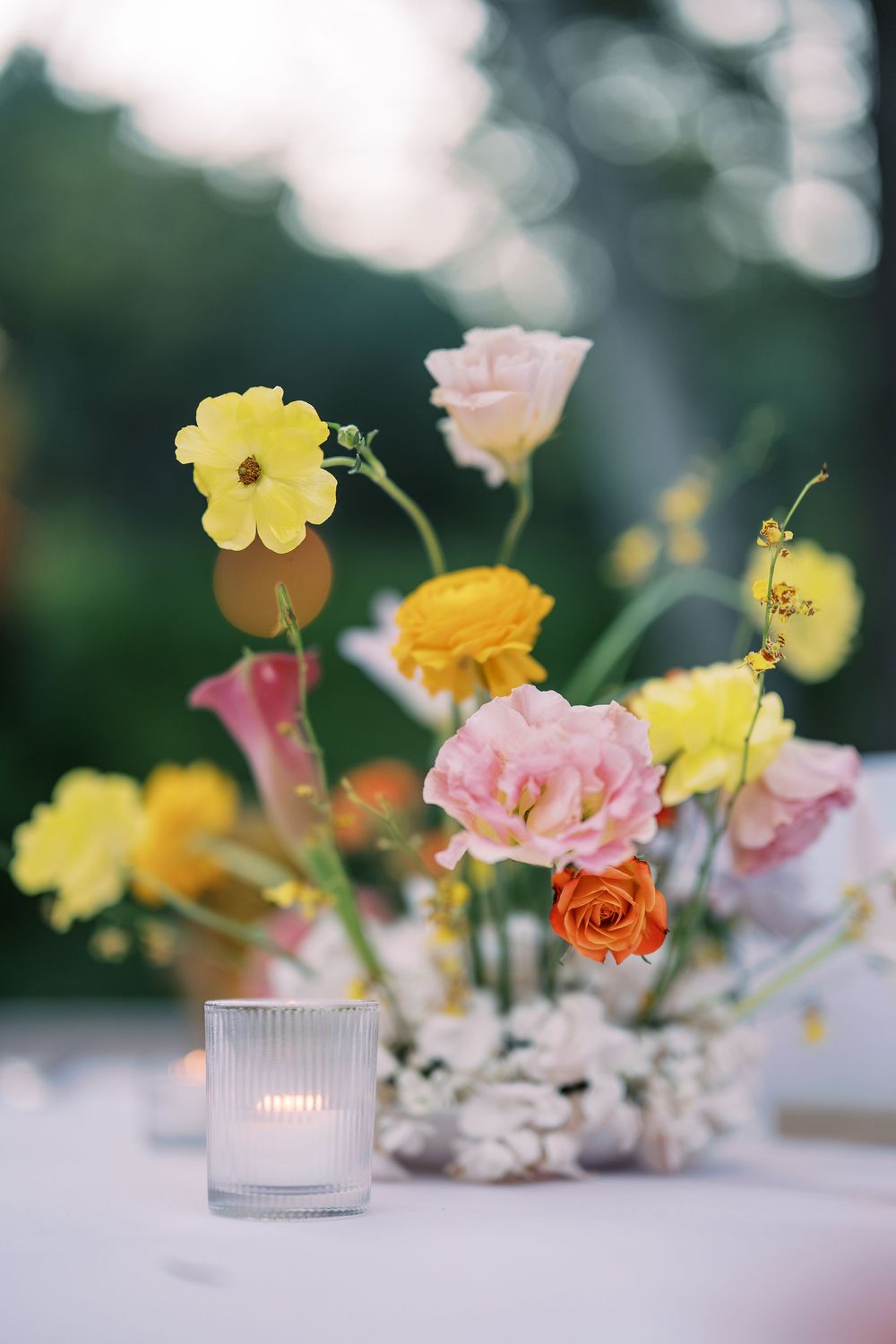 Delicate pink and yellow flowers arranged in small vases create an elegant table centerpiece at dusk.