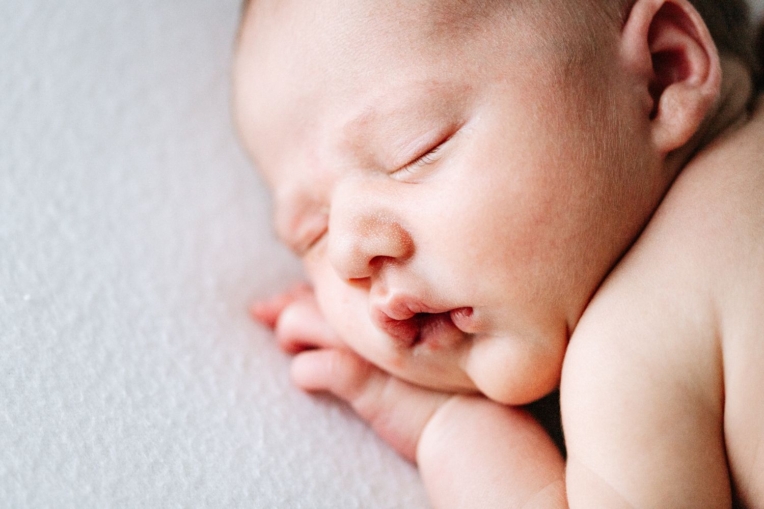 Peaceful sleeping newborn baby with soft pink skin and delicate features rests against white blanket.