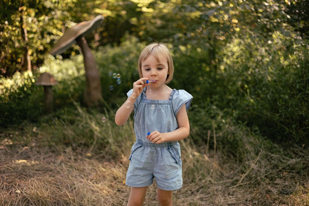 A little girl blows bubbles in a field of giant mushrooms.