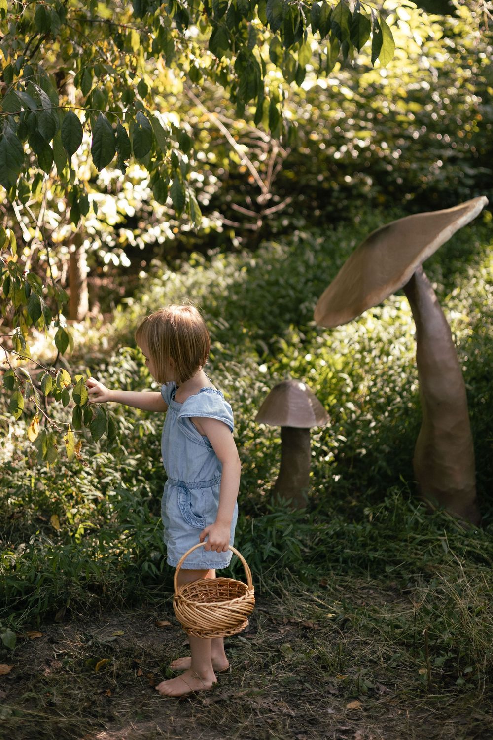 a little girl picks berries next to a giant mushroom.