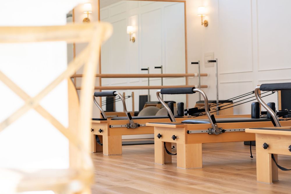 A wooden Pilates reformer machine with springs and sliding carriage in a bright studio setting.