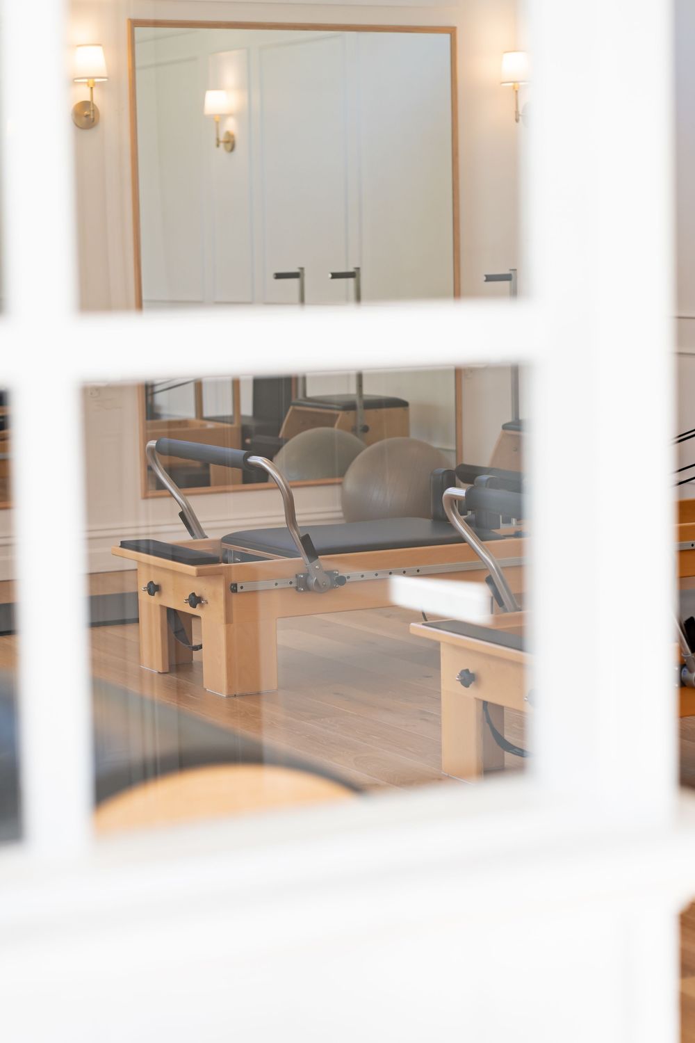 Modern pilates studio with wooden reformer machines, wall mirrors, and soft lighting creating a serene exercise environment.