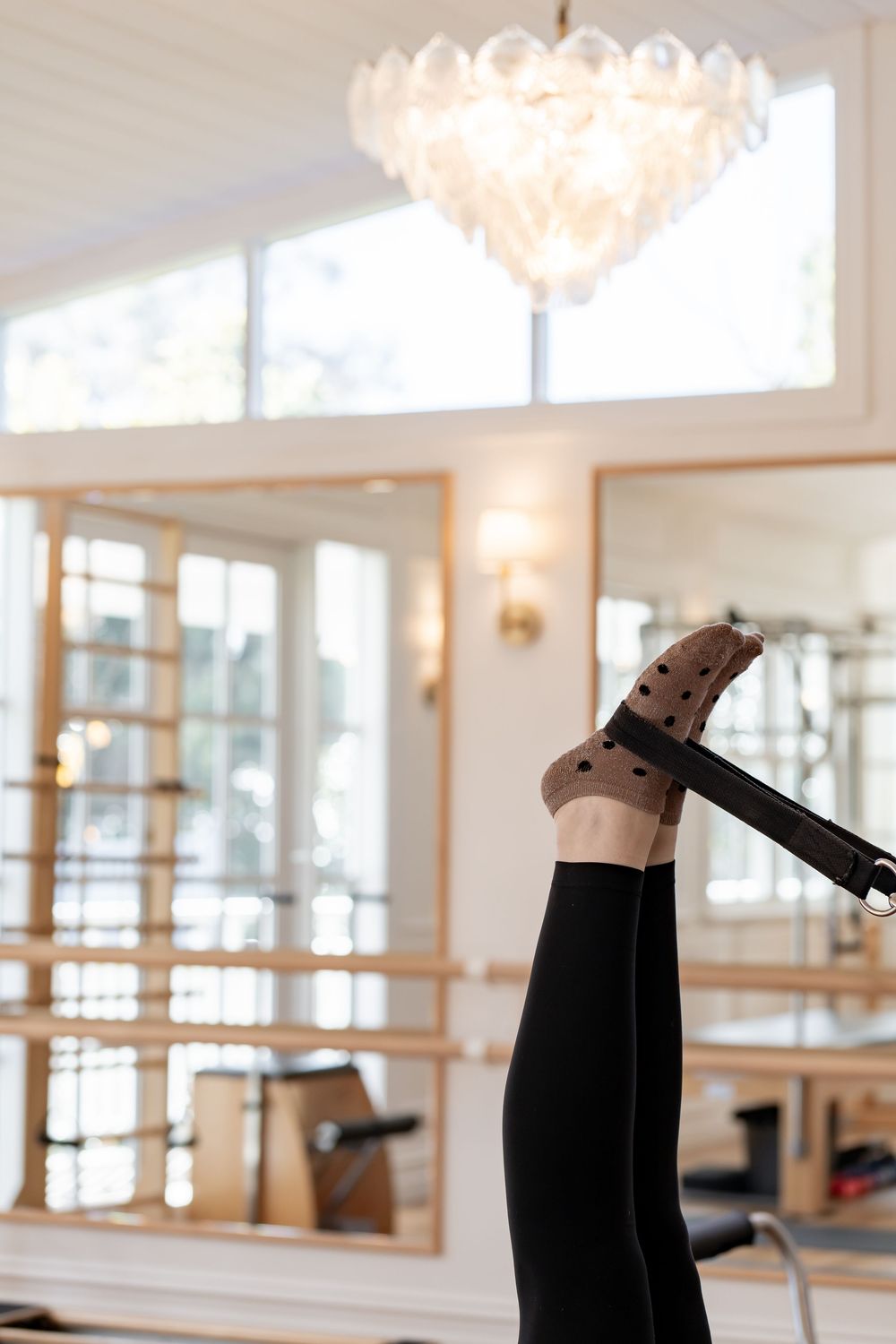 Ballet dancer practicing splits in a bright dance studio with mirrored walls and ornate chandeliers.