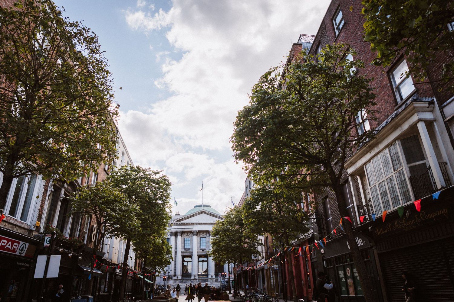 Historic brick buildings line a tree-lined street with classic architecture and autumn foliage.