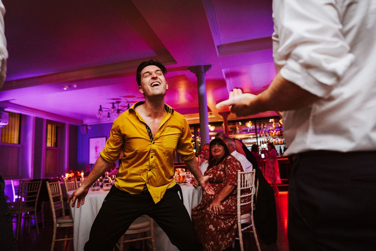 Purple-lit wedding reception dance floor with guests enjoying lively celebration.