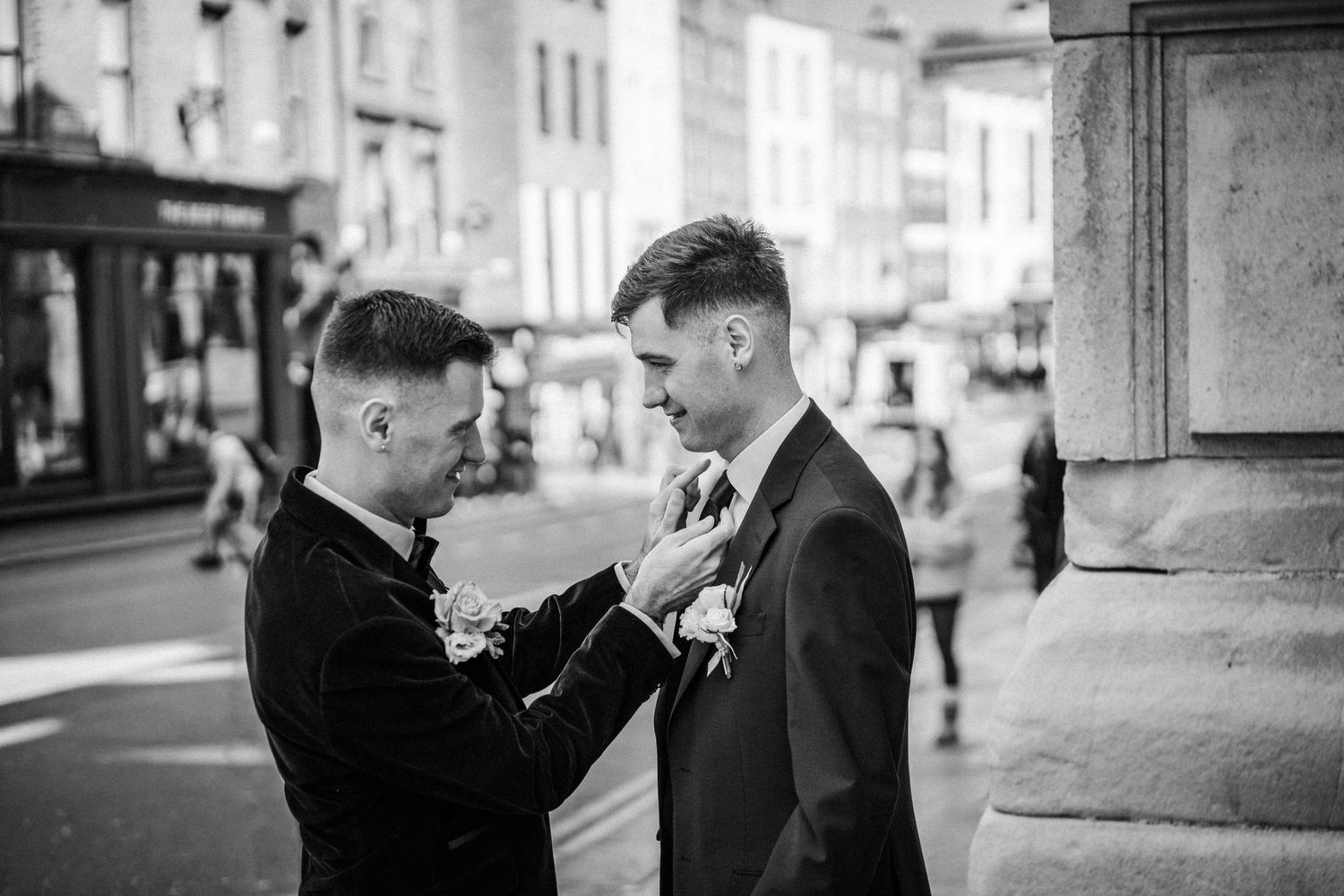 Wedding party members in formal attire sharing a lighthearted moment outside a historic building.