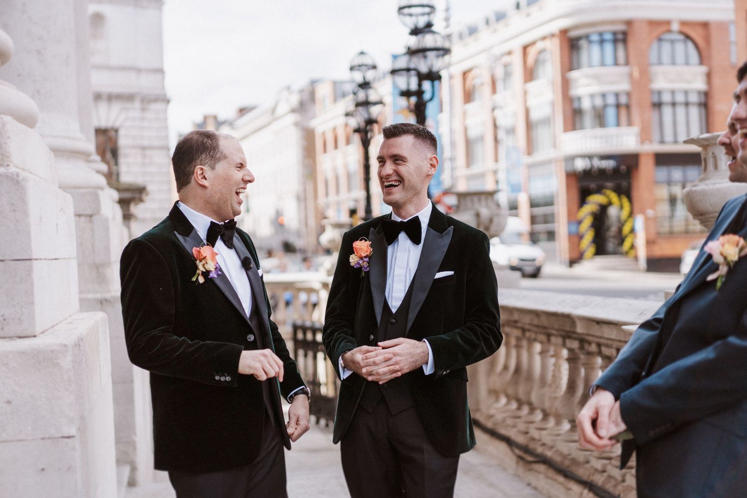 Groomsmen in black tuxedos share laughs and drinks during outdoor wedding festivities.