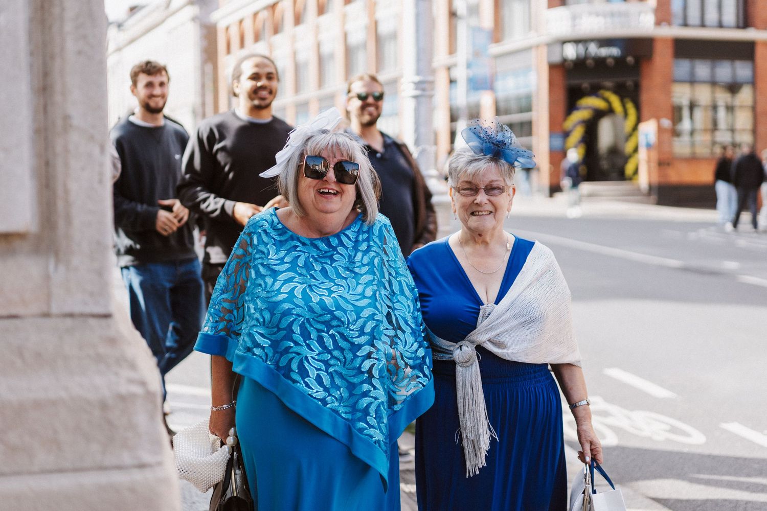 Wedding party and guests walking together along sunny urban street in formal attire.