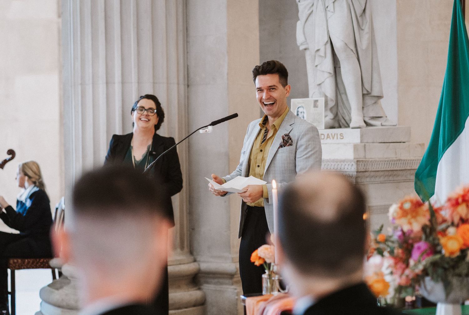 Guests gather in a grand columned hall with ornate architecture for a formal celebration.