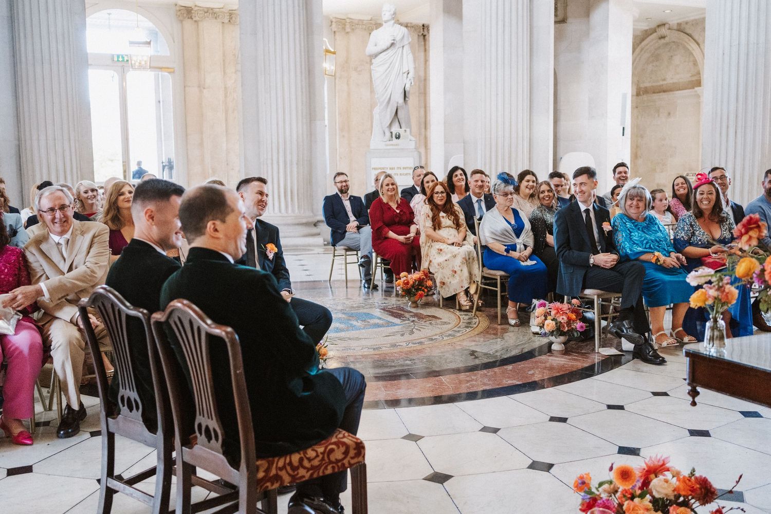 Wide angle view of wedding ceremony in classical venue with white columns and marble floors.