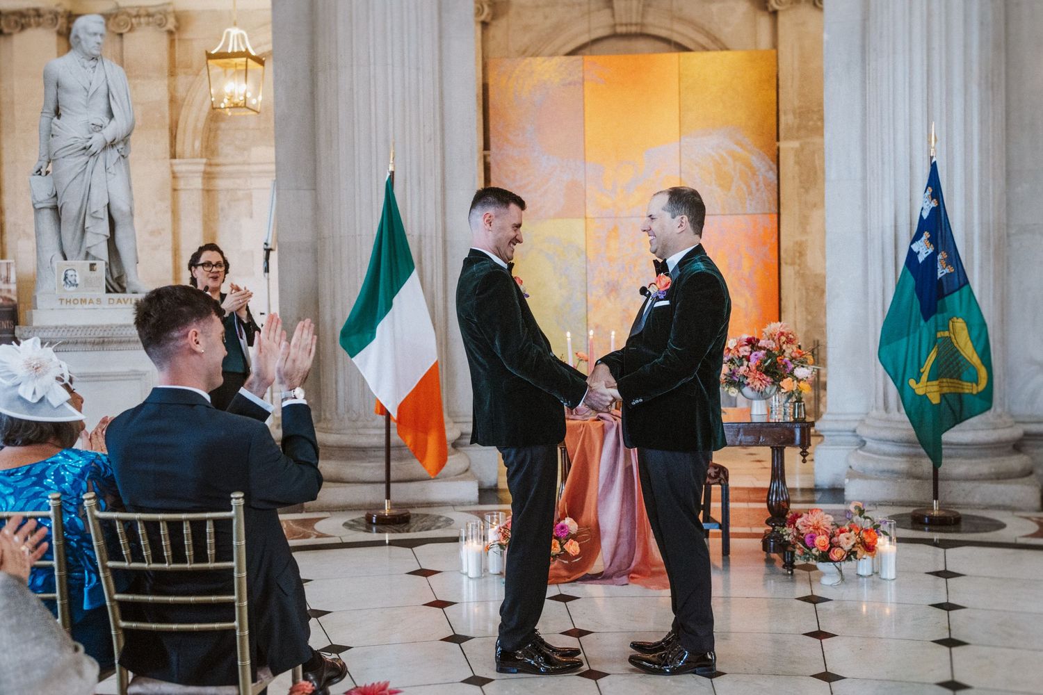 Elegant wedding ceremony setup in a historic venue with marble columns and Irish flags on display.