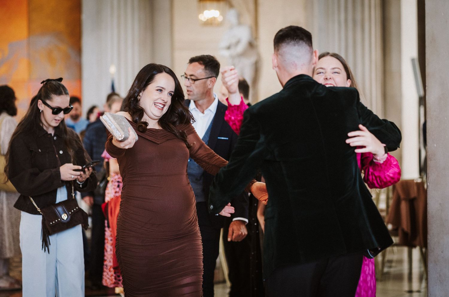Wedding celebration with guests mingling in an elegant venue with warm lighting and classical decor.