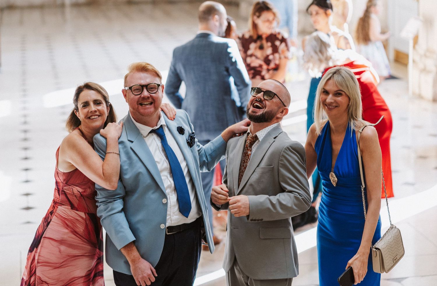 Wedding party members share joyful moments and laughter in a bright indoor venue.