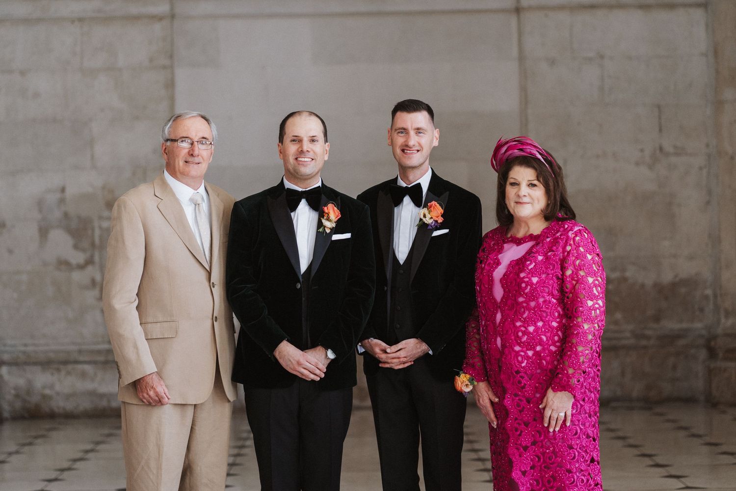 Wedding party poses together in formal attire against a stone wall background.