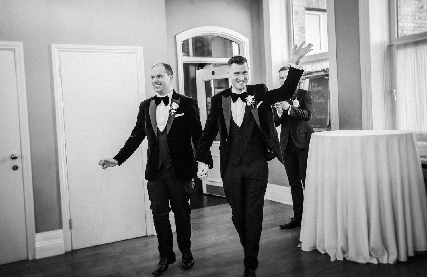 Black and white photo of formal wedding party walking through bright interior hallway.