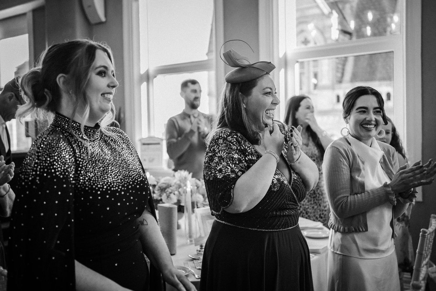 Black and white photo showing wedding guests laughing and socializing at an elegant indoor reception.