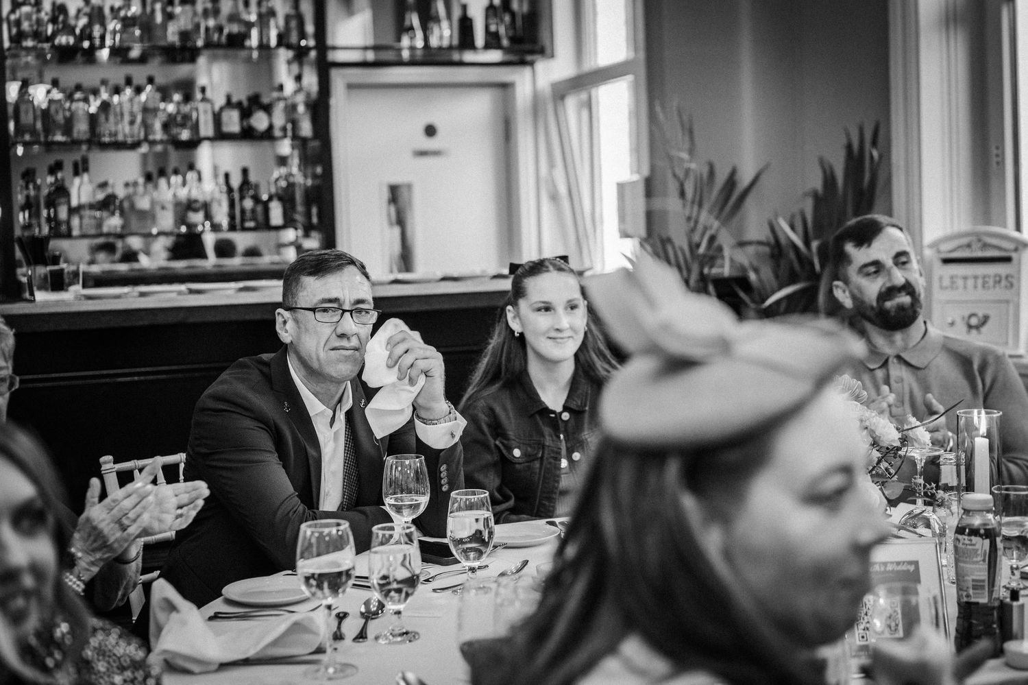 Black and white photo of wedding reception guests seated at tables with vintage-style wall decor.