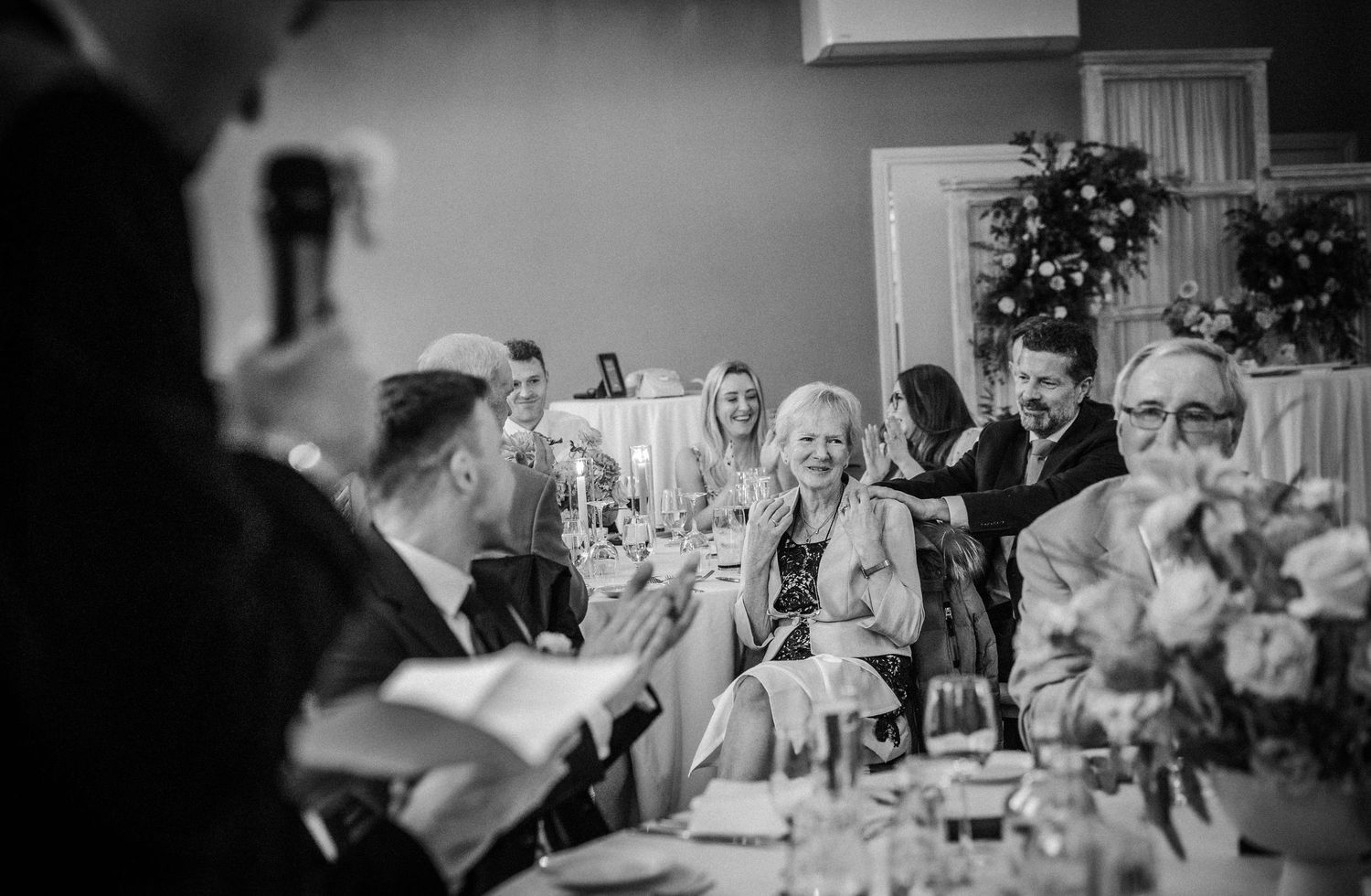 Panoramic black and white shot of wedding guests dining and celebrating at long tables.