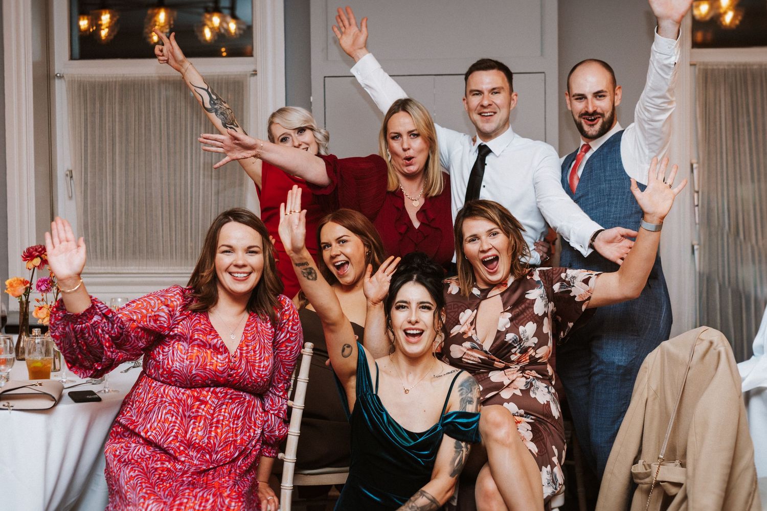 Wedding party celebrating with raised arms and joyful expressions at an indoor venue.