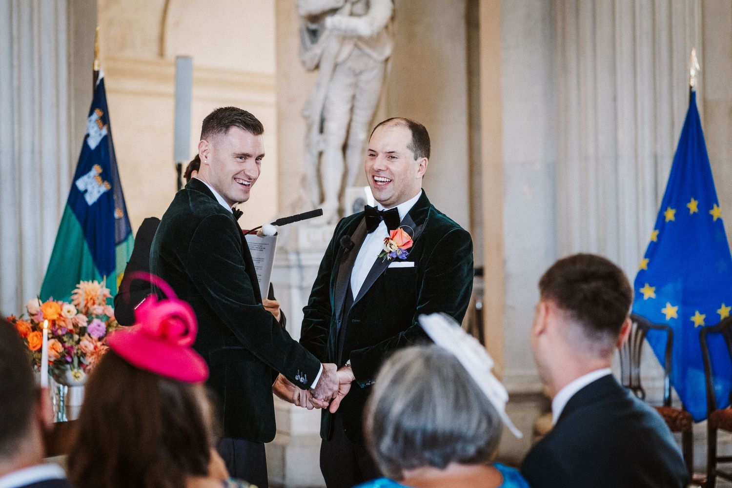 People gather in an ornate room with columns and flags during what appears to be a formal ceremony or event.