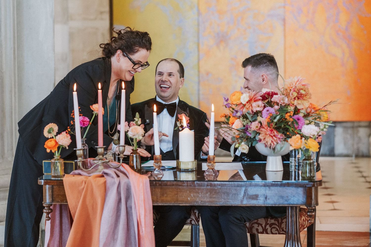 Wedding party celebrates with champagne toasts at an elegant reception with orange and pink floral decor.