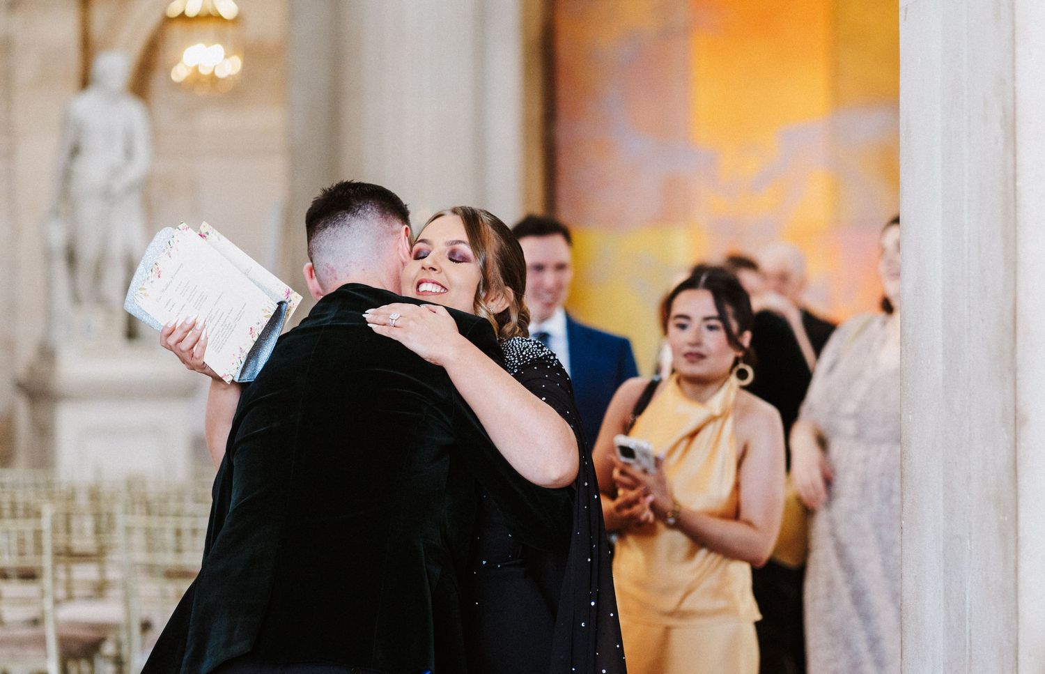 Wedding guests dance and embrace during a joyful reception celebration in an elegant ballroom setting.