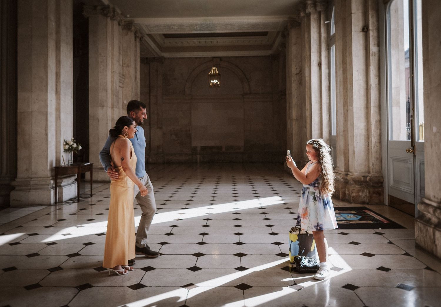 A couple dances in an elegant vintage ballroom with checkered floors and dramatic window lighting.