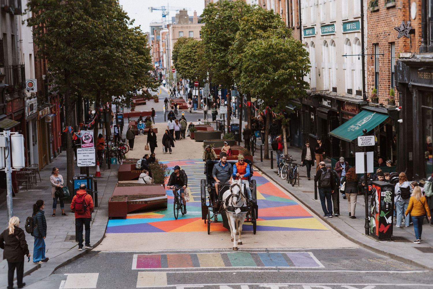 Colorful rainbow crosswalk painted on a busy urban street with pedestrians and historic brick buildings.