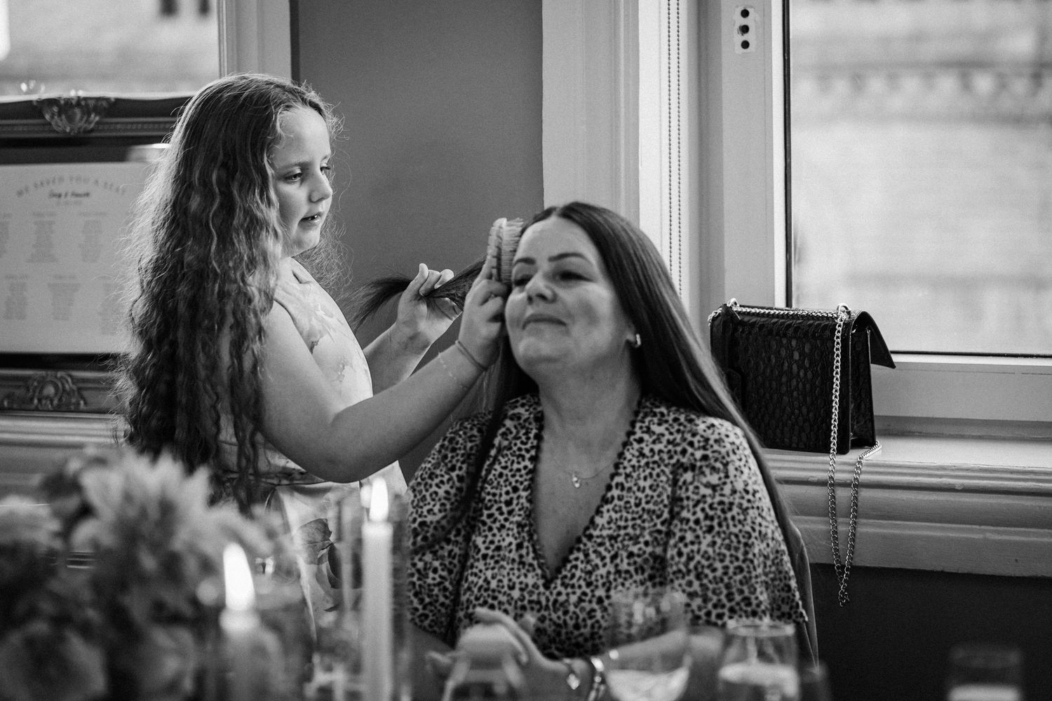 A makeup artist applies cosmetics to a client in a black and white photo by a window.