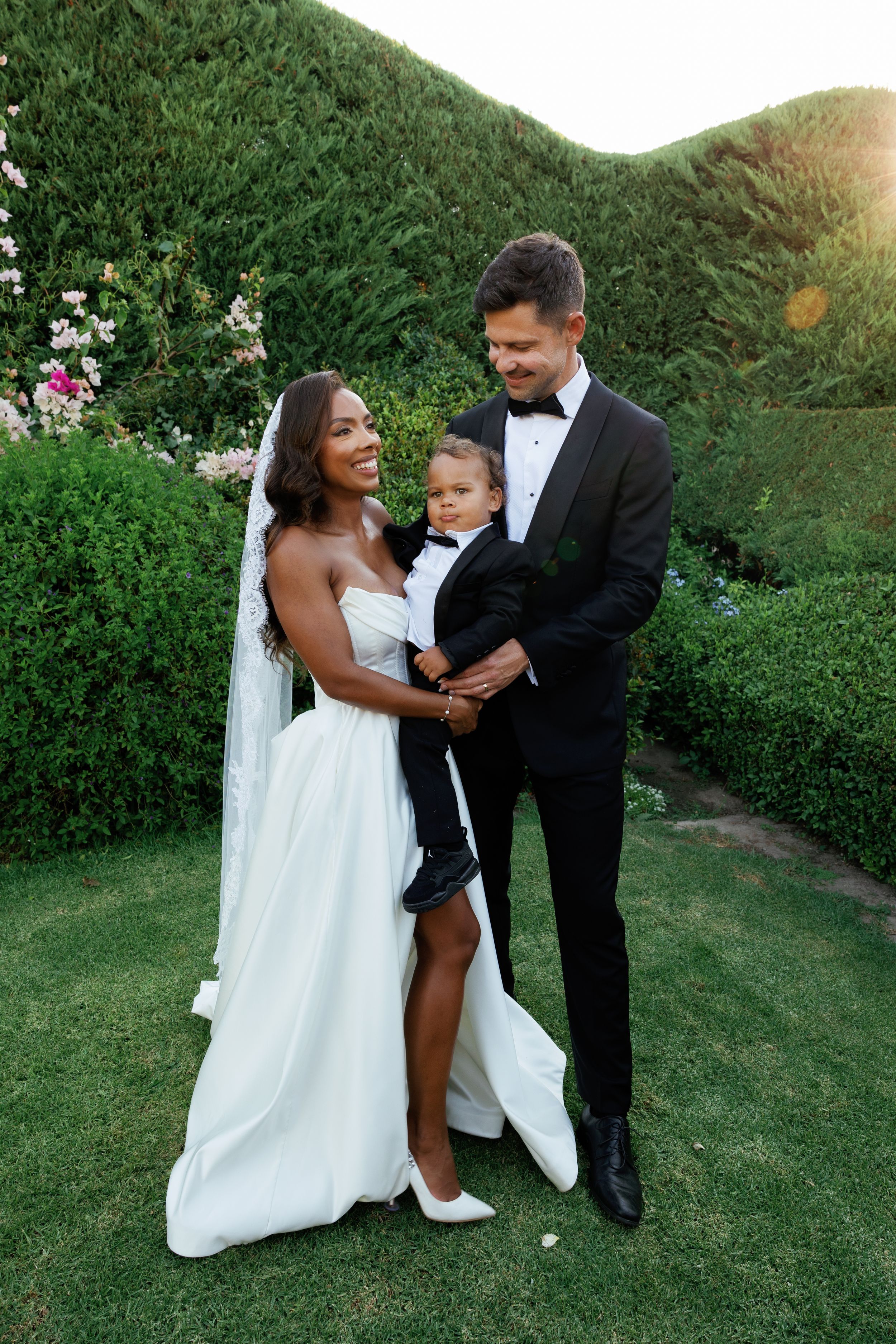 A couple in formal wedding attire share playful moments together in a lush garden setting during their special day.