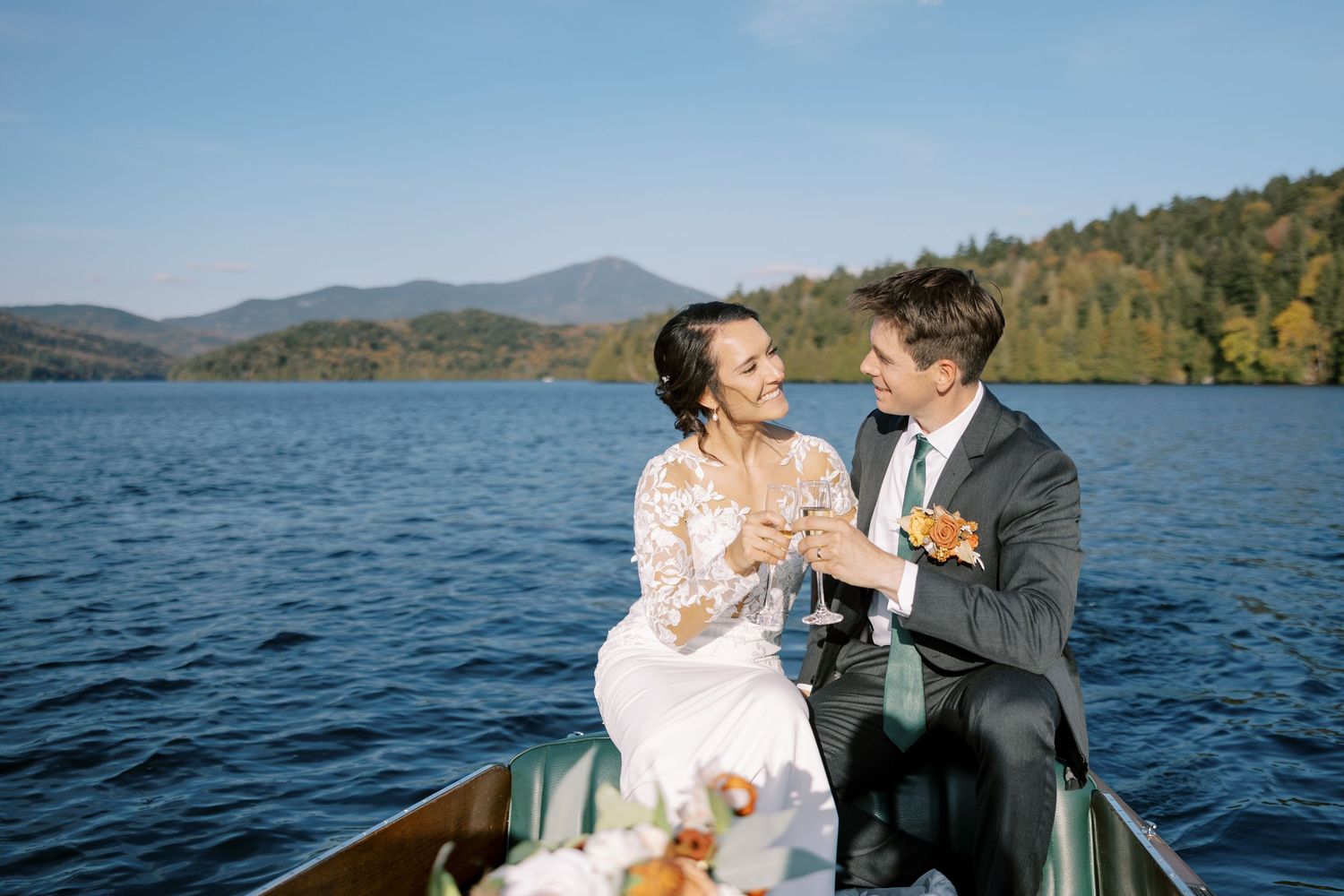 A couple shares a romantic moment on a boat during their Lake Placid wedding celebration with the Adirondack Mountains in the background.