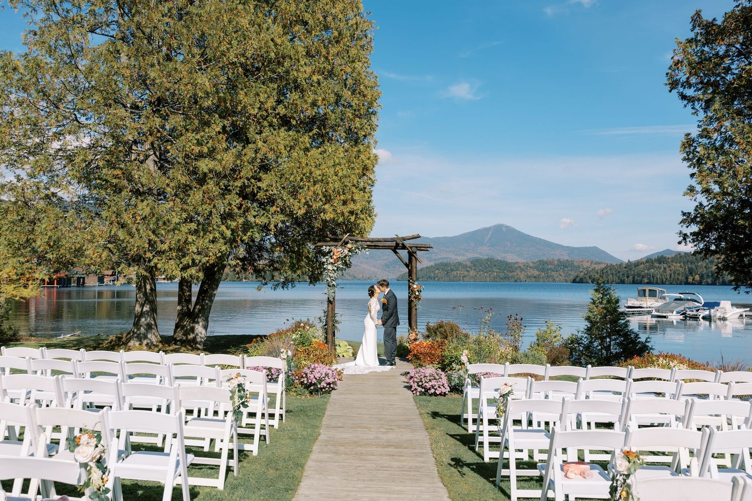 White chairs line a grassy lakeside Lake Placid wedding ceremony venue with Adirondack mountain views and boats in the distance.