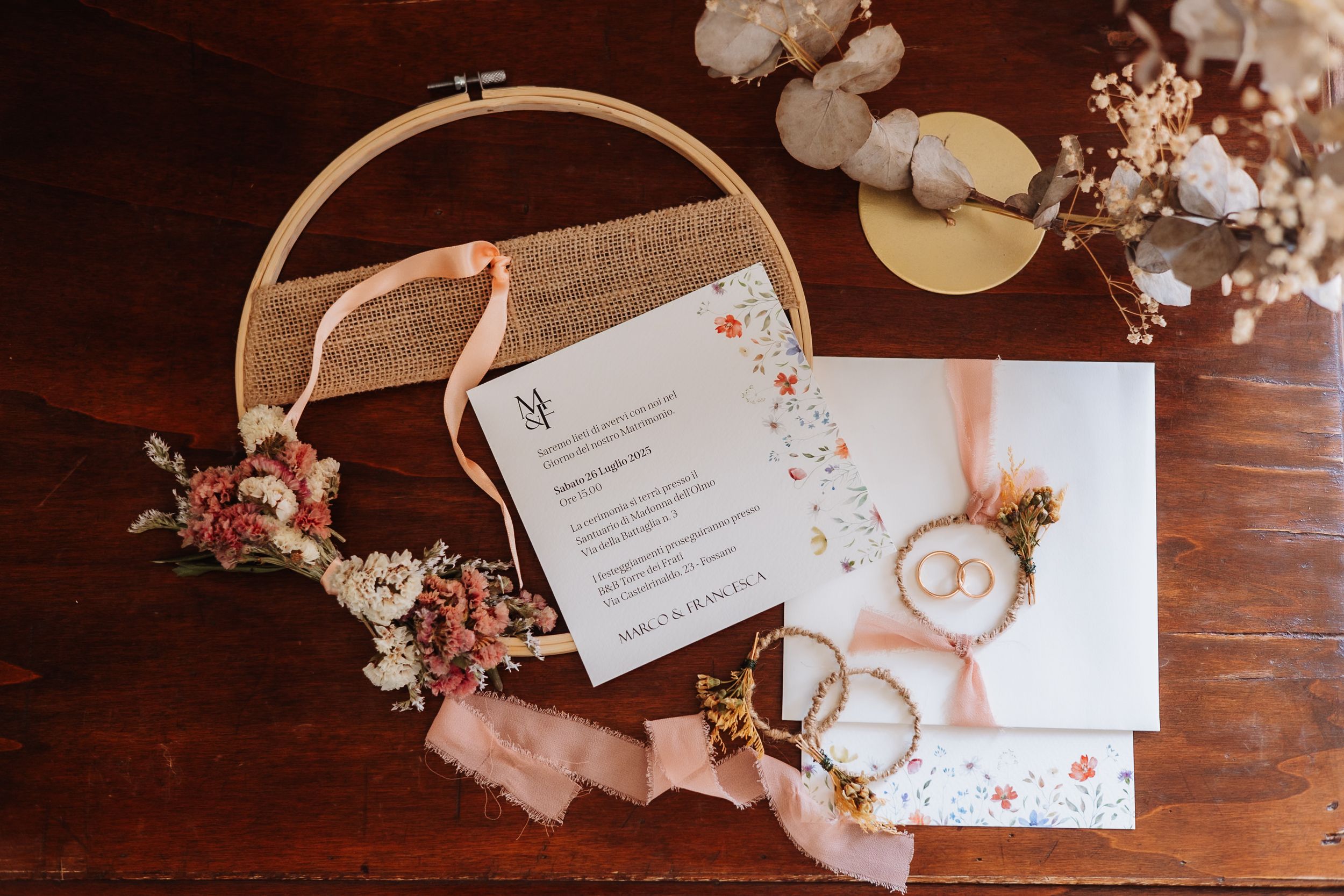 Wedding invitation cards and floral decorations arranged on dark wooden surface with soft lighting.