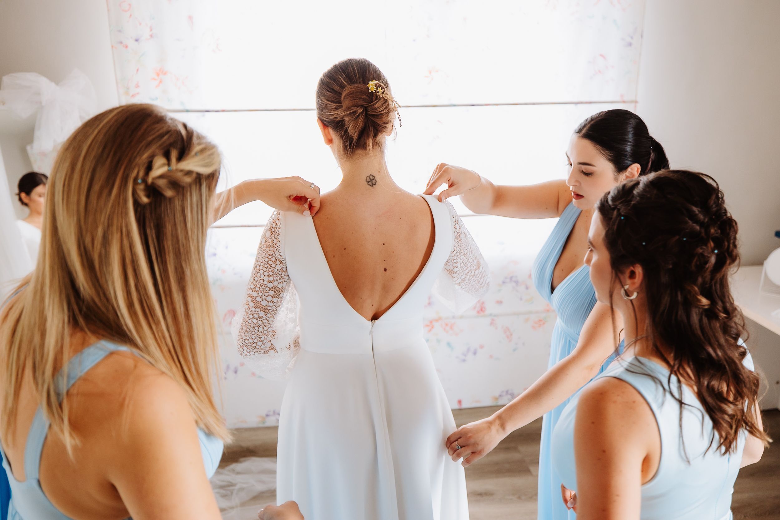 A group of bridesmaids in white robes getting ready together in a bright room before a wedding ceremony.