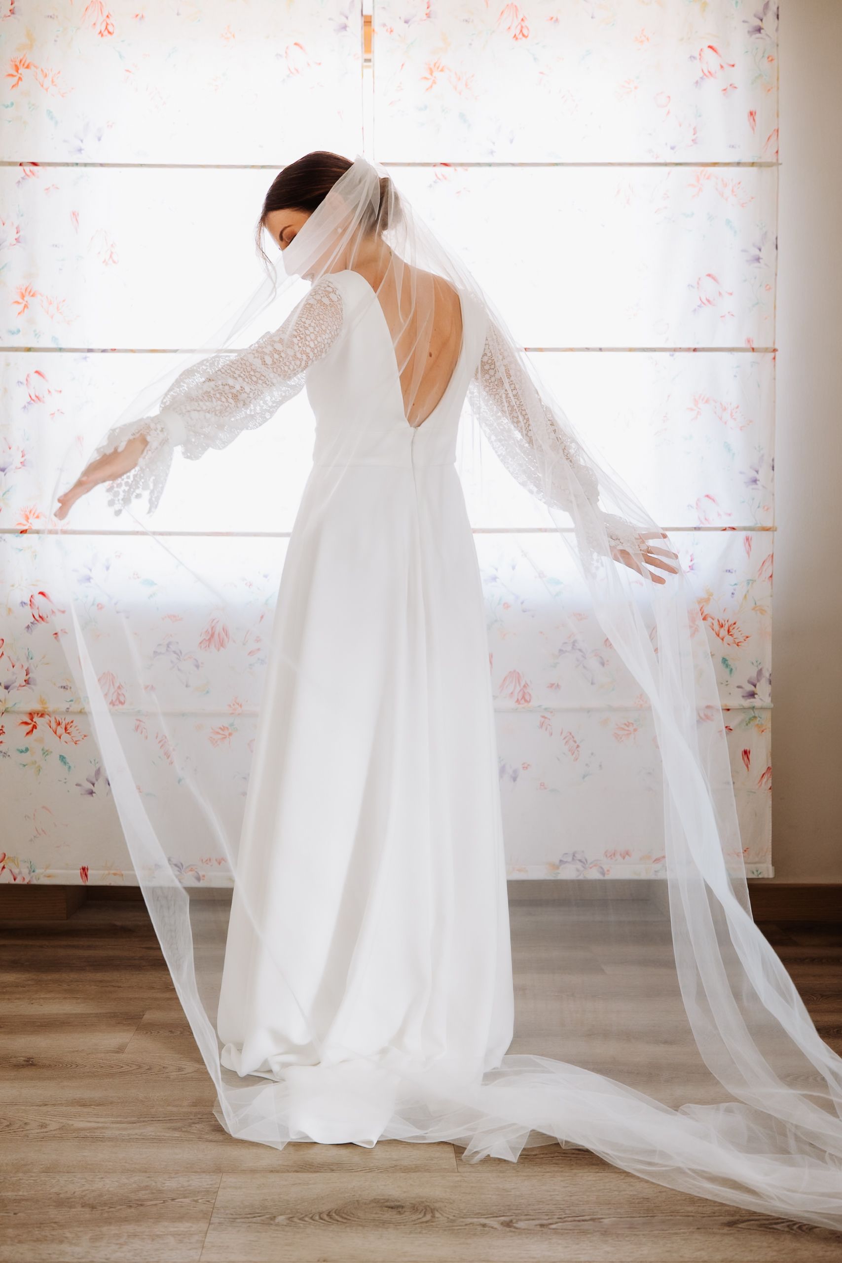 A figure in a flowing white wedding dress and veil twirls gracefully in a minimalist room with wooden floors.