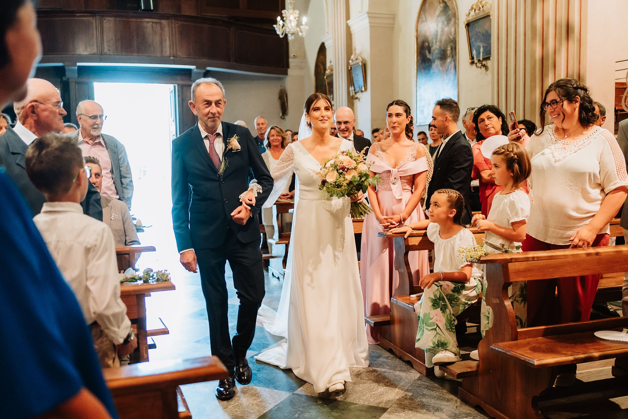 Wedding guests stand and celebrate during a joyous church ceremony with traditional wooden pews and columns.