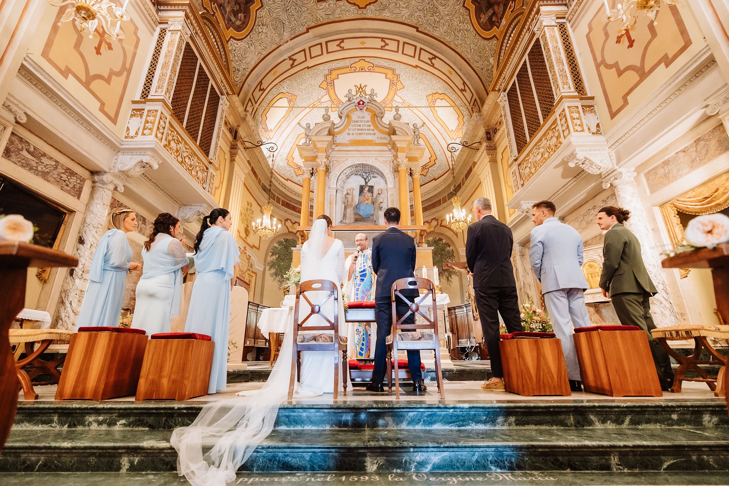 Elegant wedding ceremony in an ornate baroque church with gilded details and frescoed ceilings.