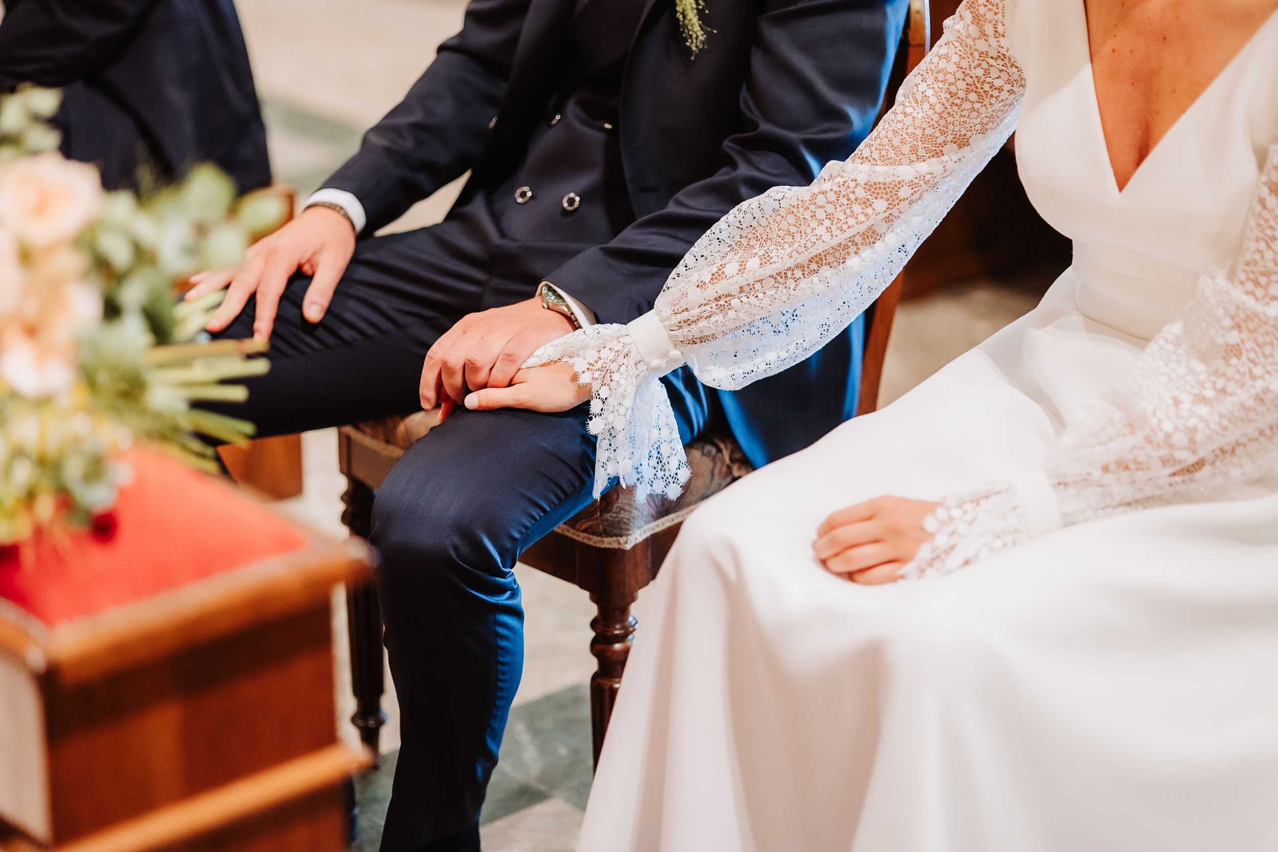 Close-up view of hands holding during a wedding ceremony in formal attire.