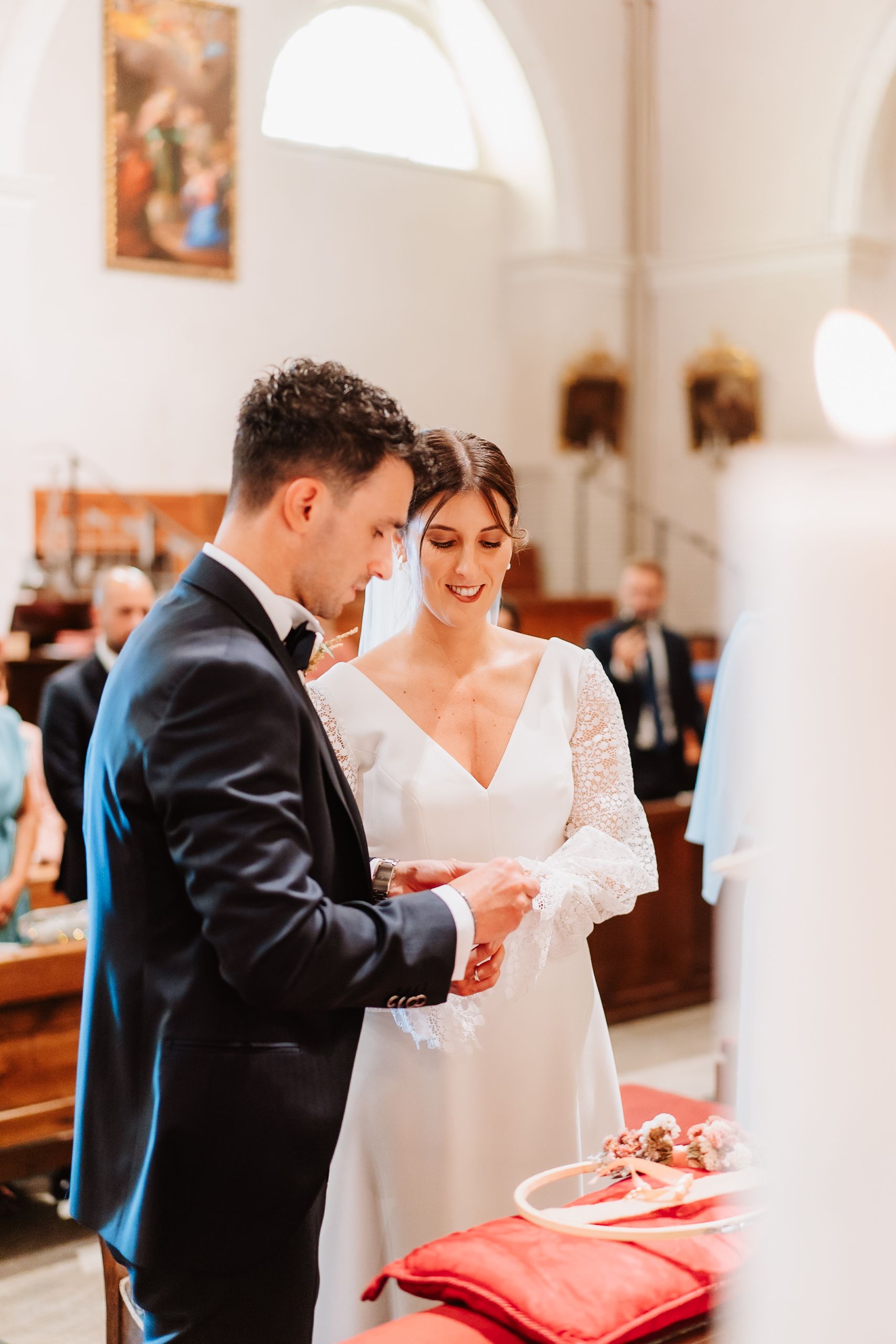 Couple participates in a traditional wedding ceremony ritual inside a bright white church interior.