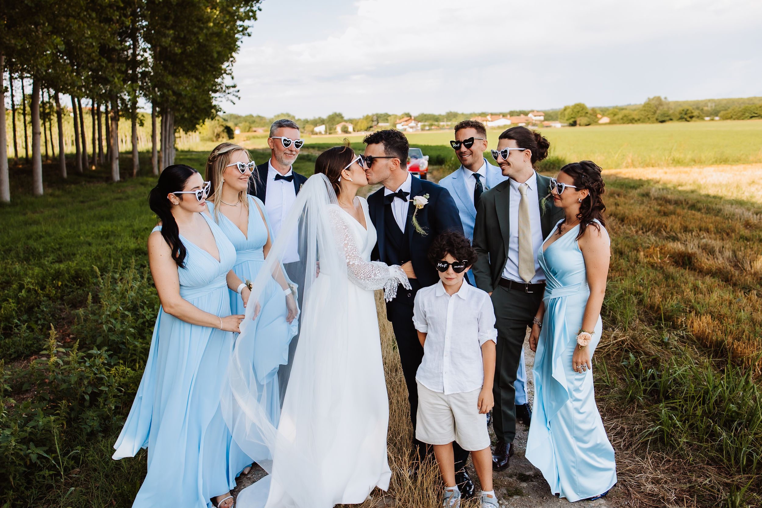 Wedding party in light blue dresses and formal attire poses together in a scenic outdoor field.