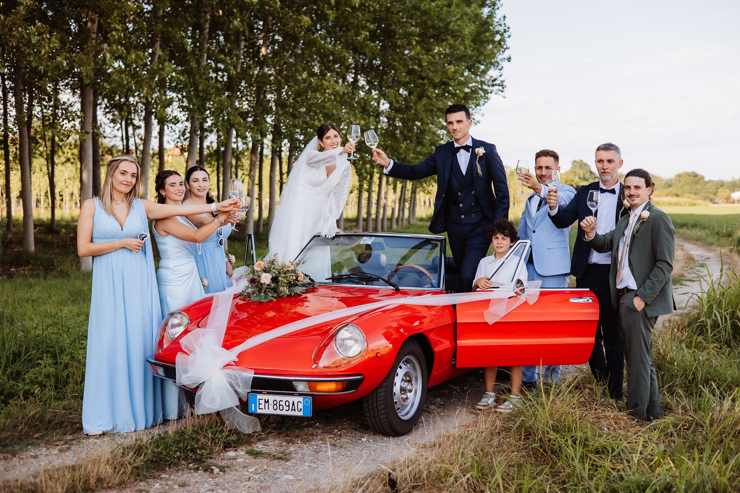 A classic red Ferrari sports car parked in a scenic outdoor setting during a wedding celebration.