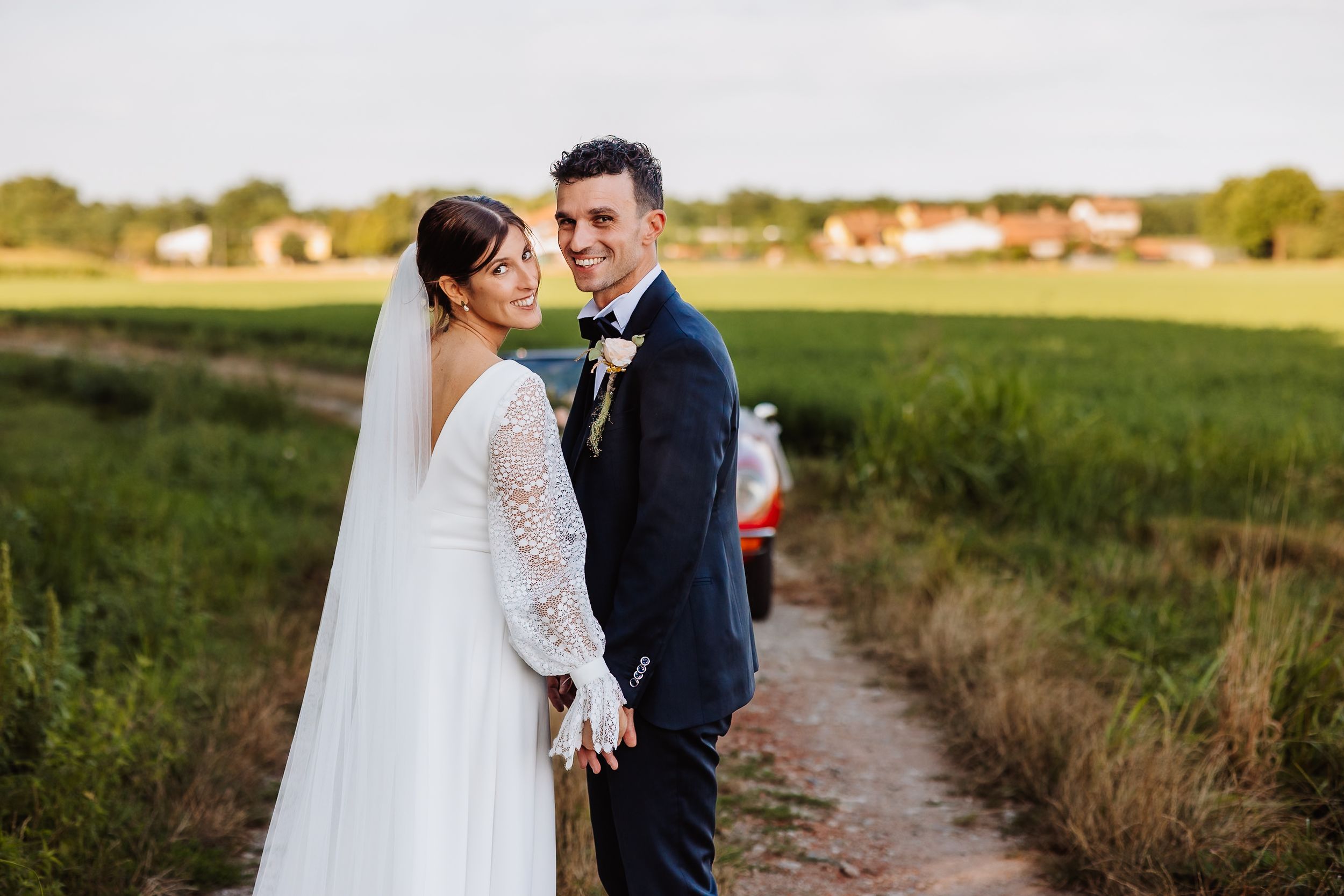 Couple in wedding attire embraces in golden sunlit field during sunset photo session.