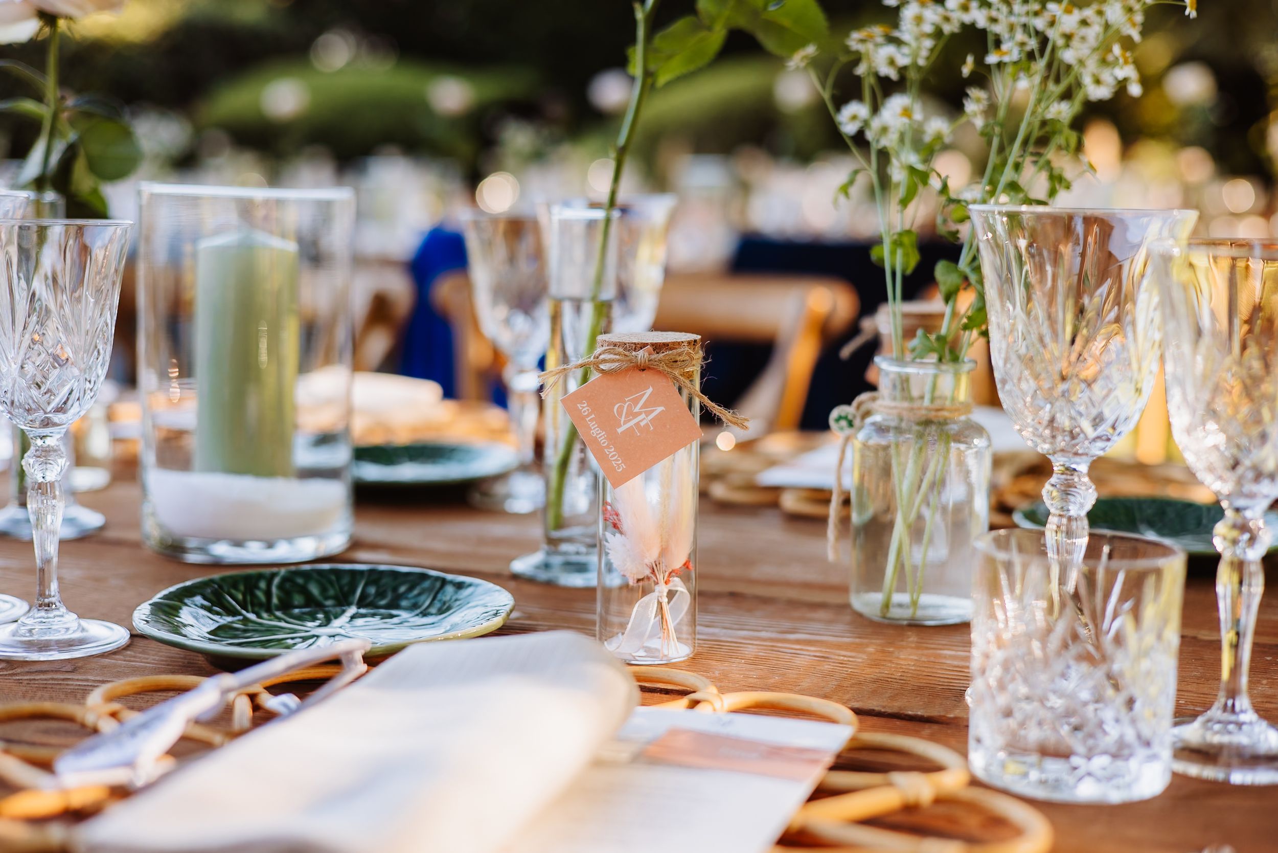 Crystal glassware and elegant table settings arranged on a rustic wooden table for an outdoor event.