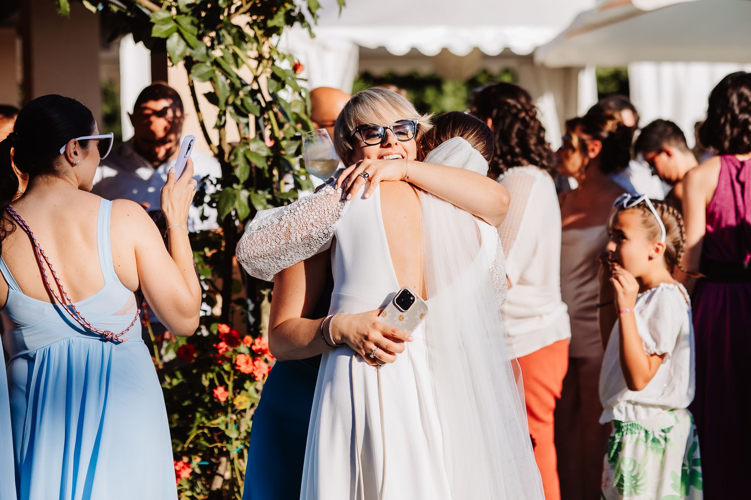 Guests celebrate at an outdoor wedding reception with people embracing and mingling in a garden setting.