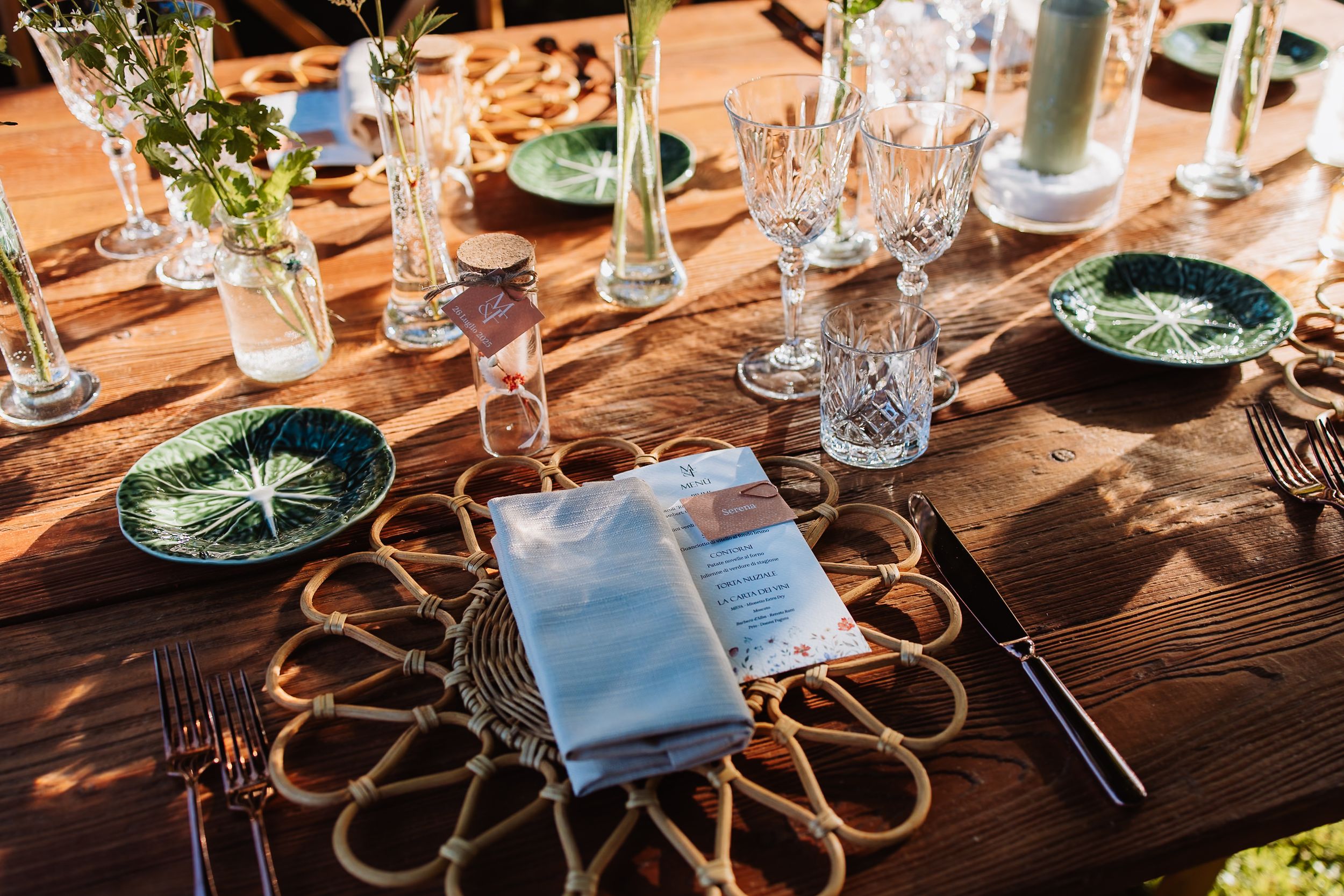 Elegant table setting with crystal glasses and green plates on rustic wooden surface with woven placemats.