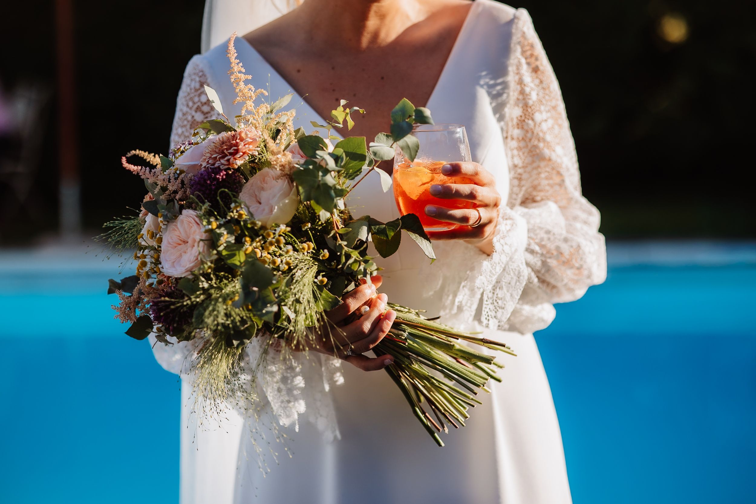 A close-up shot of a bridal bouquet with wildflowers and greenery against a bright turquoise blue background.