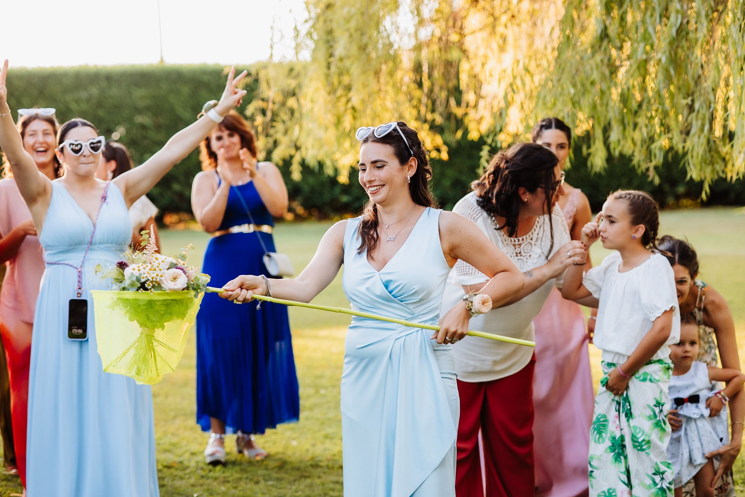 Wedding party celebrating outdoors with joyful dancing and colorful dresses in golden sunlight.