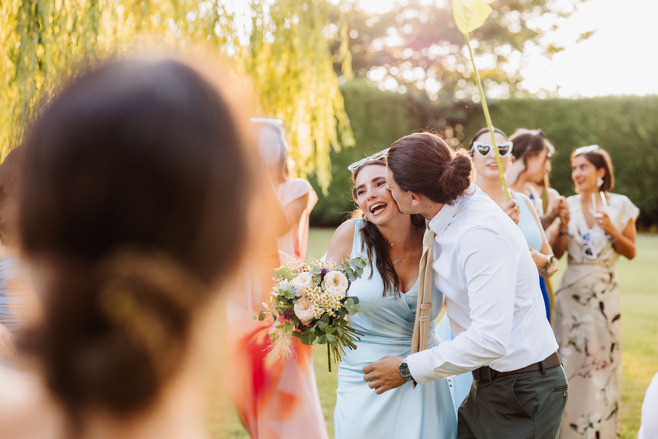 Wedding party celebrating outdoors at sunset under a willow tree.