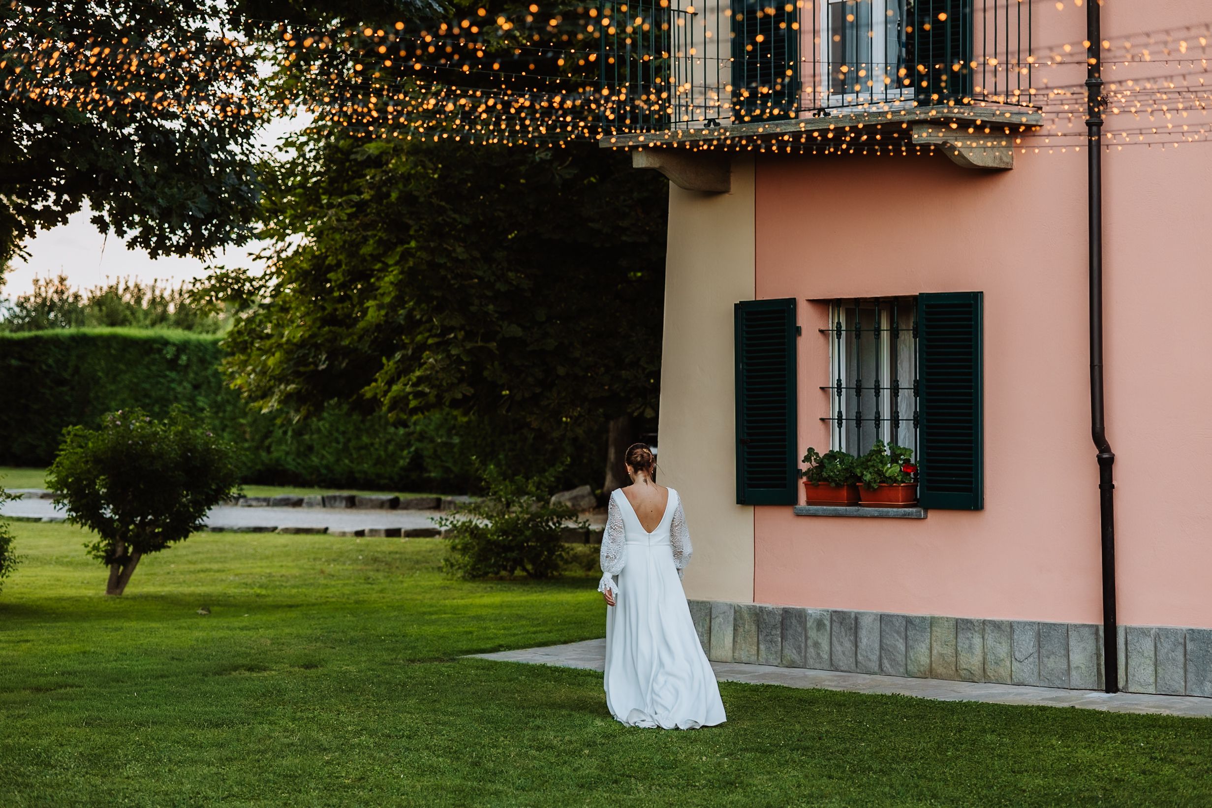 Pink stucco building facade with string lights and greenery creating a romantic wedding venue atmosphere.